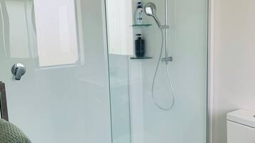 A modern bathroom with a glass-enclosed shower, a toilet, and a towel rack.