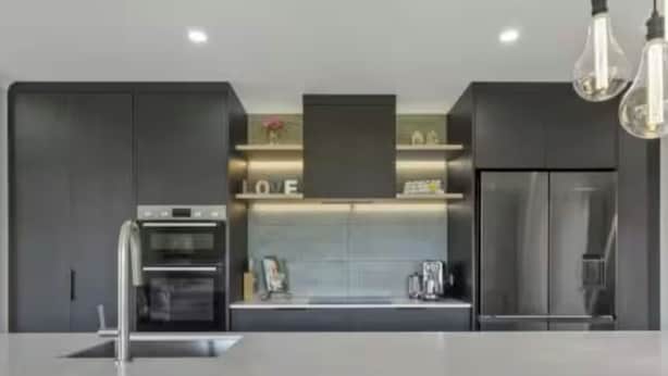 A modern kitchen with dark cabinetry, a central island, and pendant lighting. - Modern & Spacious 2yo Home (New Plymouth)