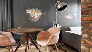 Un comedor moderno con una mesa redonda de madera, dos sillas tapizadas en rosa, una lámpara de pie y un sofá gris.