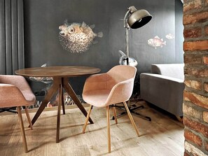 A modern dining area with a round wooden table, two pink upholstered chairs, a floor lamp, and a gray sofa.