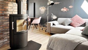 Una sala de estar moderna con un estufa de leña negra, un sofá gris con cojines, una mesa de comedor de madera y una silla.