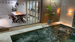 A modern indoor pool area with a glass partition, a dining table with chairs, and a potted plant.