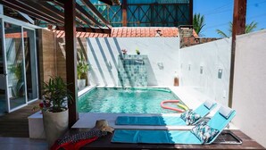 A private pool with a waterfall feature, surrounded by a white wall and a wooden deck.
