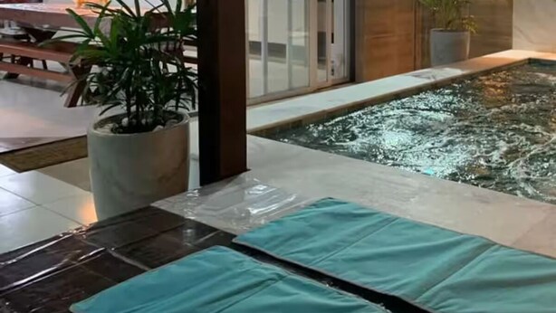 A modern indoor pool area with a water feature, potted plants, and a dining area with a table and chairs.