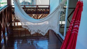 A hammock in a wooden-floored corridor with a view of a balcony and a red curtain.