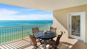 Ein Balkon mit rundem Tisch und Stühlen, eine Tür mit Fenster und Blick aufs Meer.