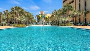 Ein klares, blaues Schwimmbecken, umgeben von Palmen und einem Gebäude mit Balkonen.