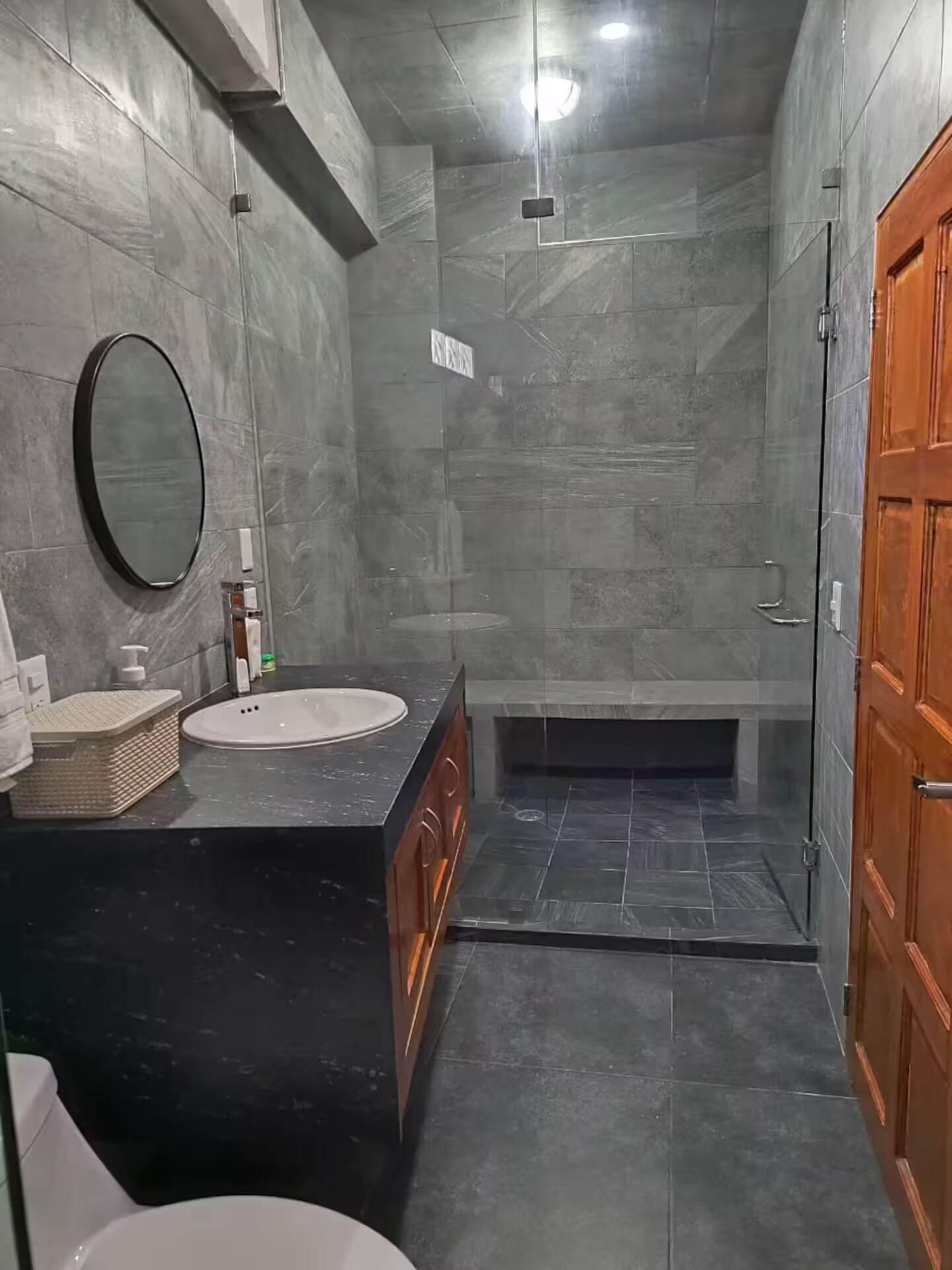 Uma casa de banho moderna com lavatório de mármore preto, um espelho redondo e porta de madeira.