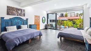 A modern bedroom with two beds, a balcony with plants, and a city view.