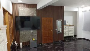 A modern interior with a large flat-screen TV mounted on a wall, a wooden door, a marble fireplace, and a white dresser with drawers.