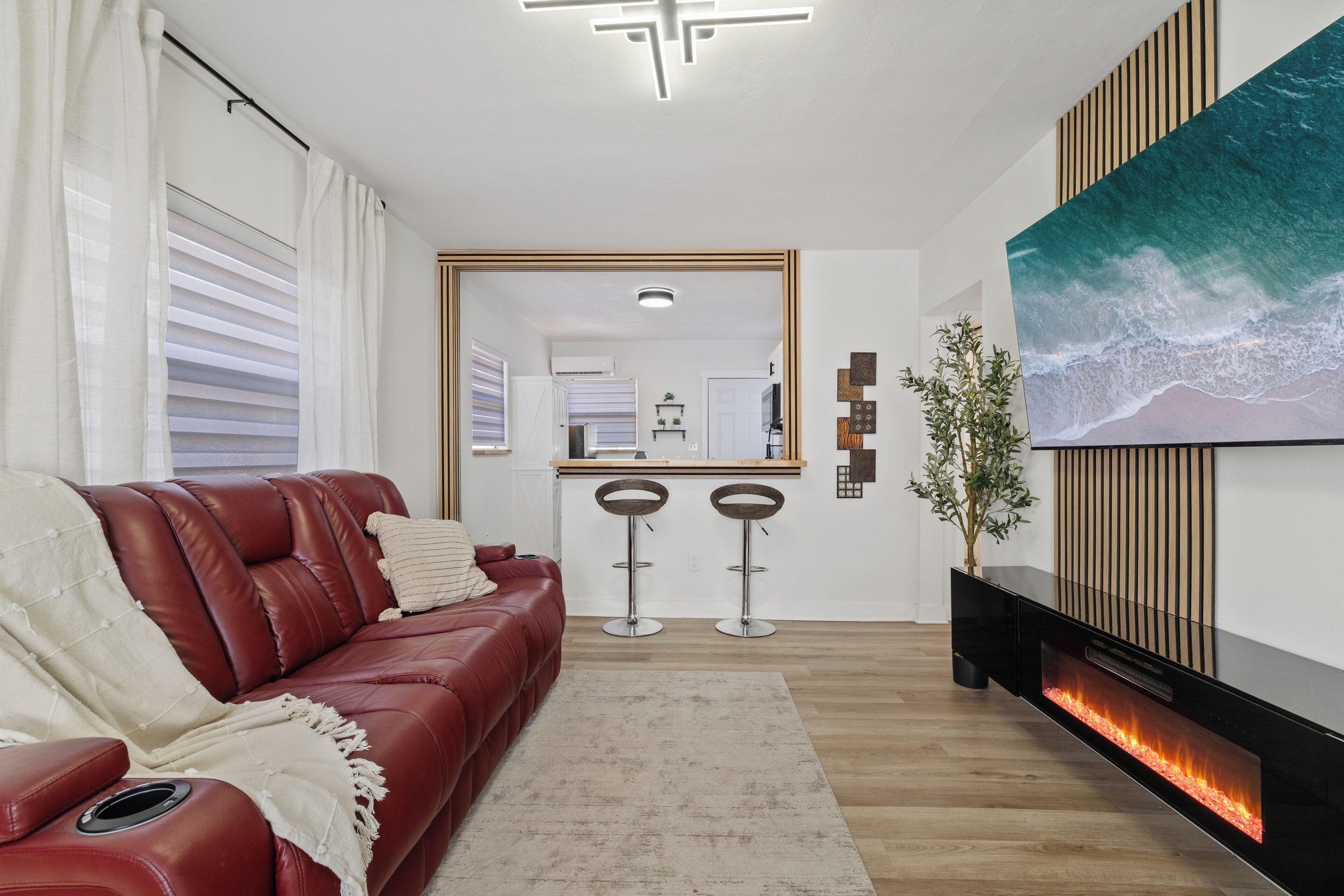 Una sala de estar moderna con un sofá de cuero rojo, un televisor de pantalla plana grande, una chimenea y una cocina al fondo.