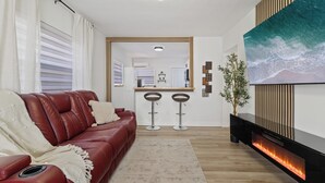 A modern living room with a red leather sofa, a large flat-screen TV, a fireplace, and a kitchen in the background. - Kick back and relax in this calm, stylish home! Close to downtown, beaches, park (St. Petersburg)