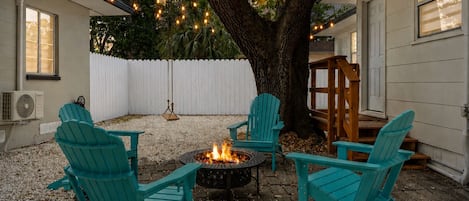 A backyard with a fire pit, outdoor seating, and string lights.