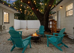 A backyard with a fire pit, outdoor seating, and string lights.