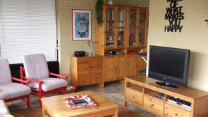 Een woonkamer met een televisie, houten kasten, een rode stoel en een lijst met een foto aan de muur.