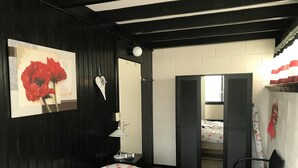 Een slaapkamer met een bed, nachtkastje, lamp, spiegel en een deur naar een andere kamer.