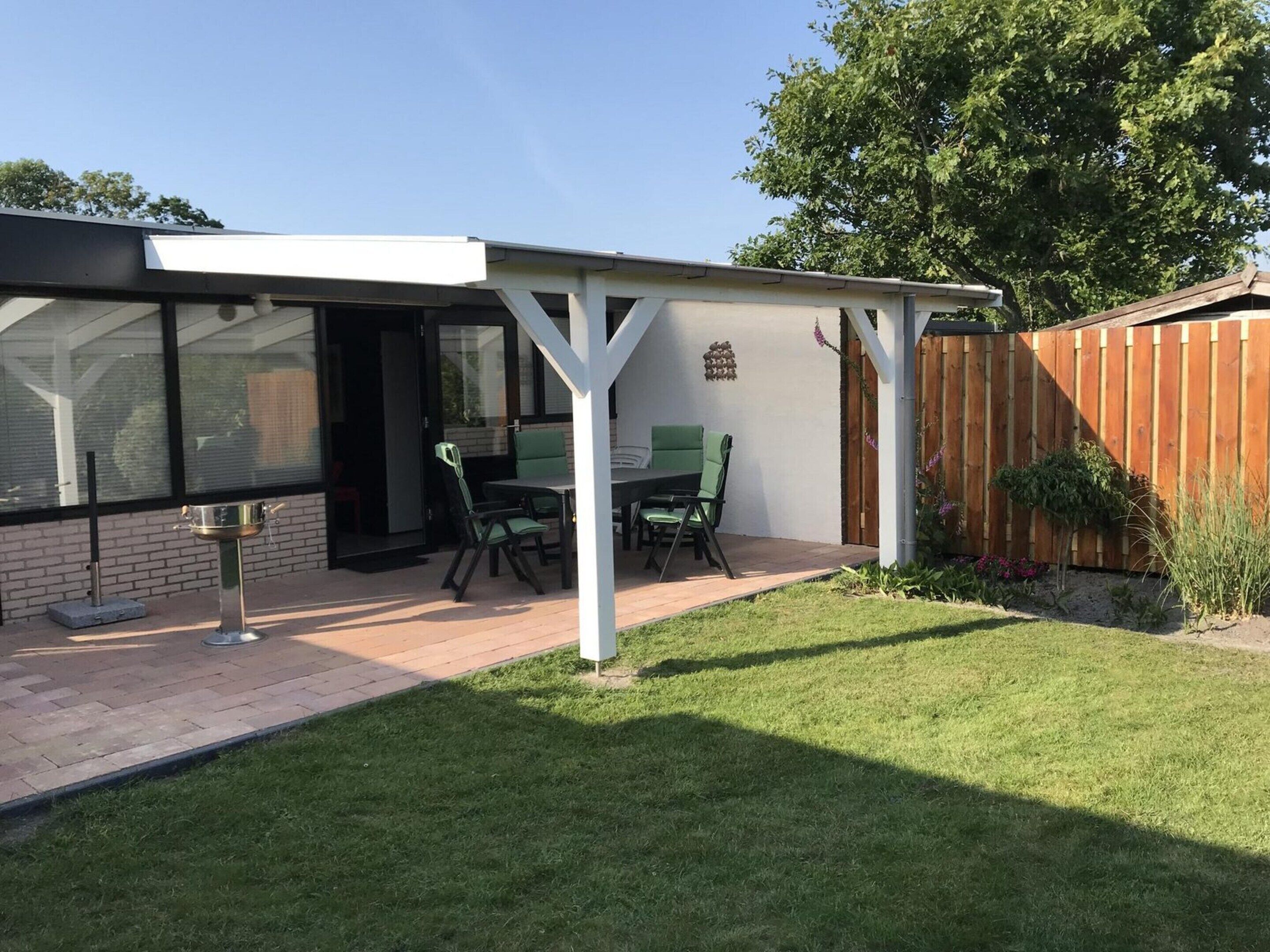 A patio with a table and chairs, a pergola, a wooden fence, and a grassy lawn.