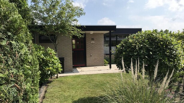 Een modern huis met een bakstenen gevel, een zwarte deur en een kleine voortuin met gras en planten.