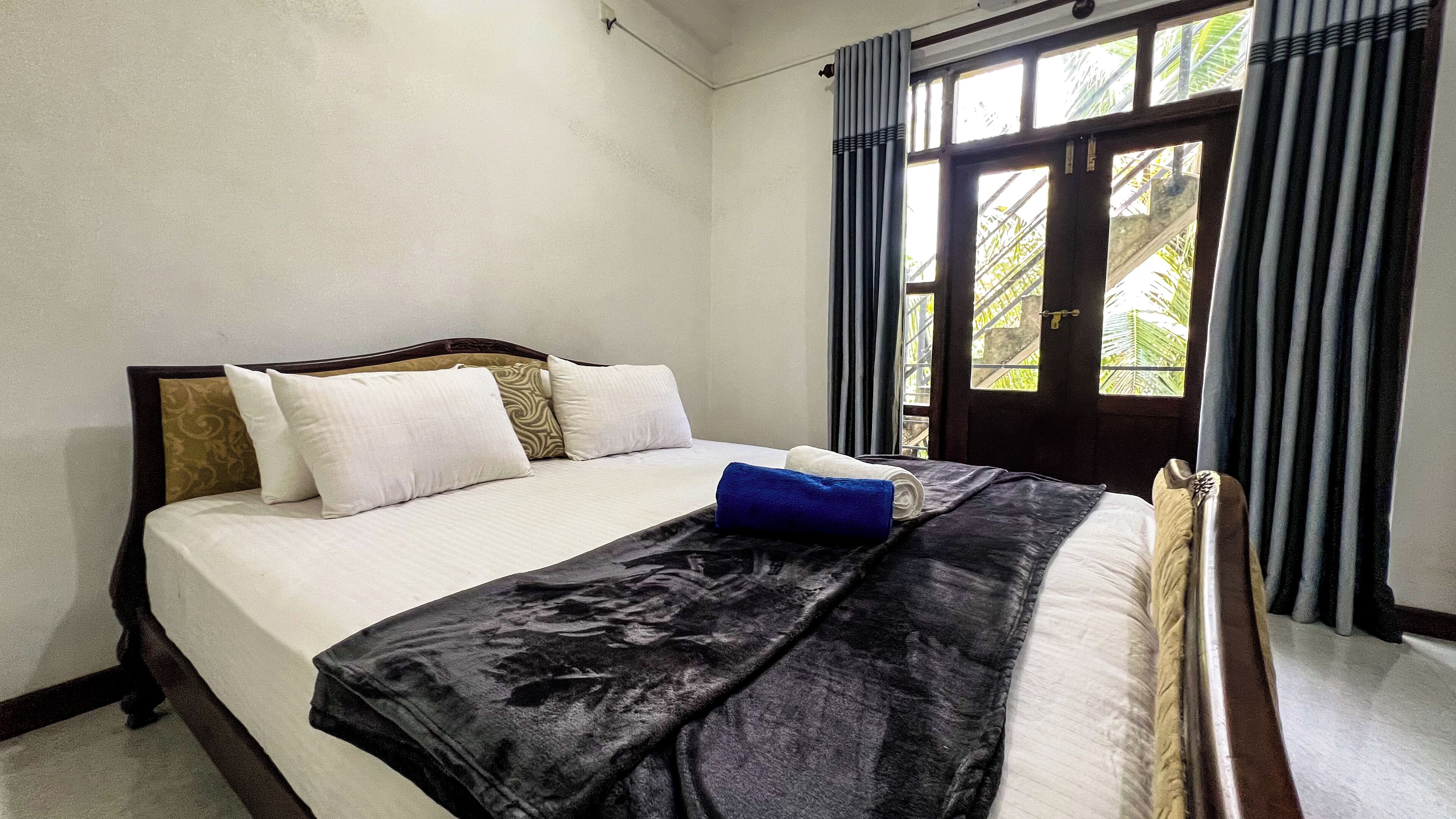 A neatly made bed with white and patterned pillows, a dark blanket, and a blue towel.