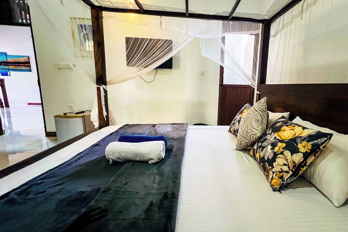 Un lit bien fait, avec une couverture bleue, une serviette blanche et des coussins à motifs floraux.
