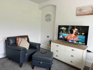 Un salon avec un canapé en cuir, un pouf et un téléviseur posé sur un meuble en bois.