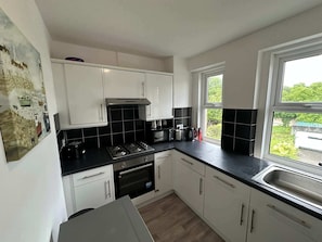Une cuisine avec des meubles blancs, un plan de travail noir, une cuisinière à gaz, un four et une fenêtre donnant sur un beau paysage.