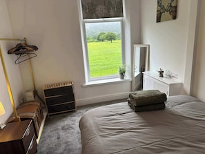 Une chambre à coucher comprenant un lit, une commode, un miroir, une fenêtre donnant sur un champ verdoyant et un radiateur.