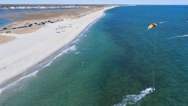 Une plage aux eaux cristallines, avec un parachute ascensionnel visible au loin.