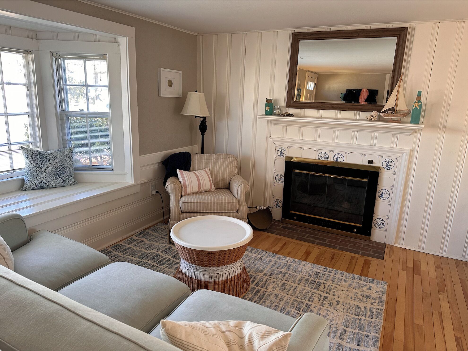 A cozy living room with a fireplace, a sofa, a chair, and a window with blinds.