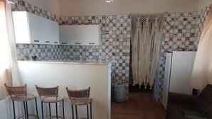 Una cocina con encimera blanca, tres taburetes de mimbre, un sofá marrón y baldosas estampadas en las paredes.