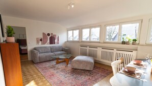 Una sala de estar moderna con un sofá gris, una mesa de centro de cristal y una zona de comedor con mesa preparada para cuatro.