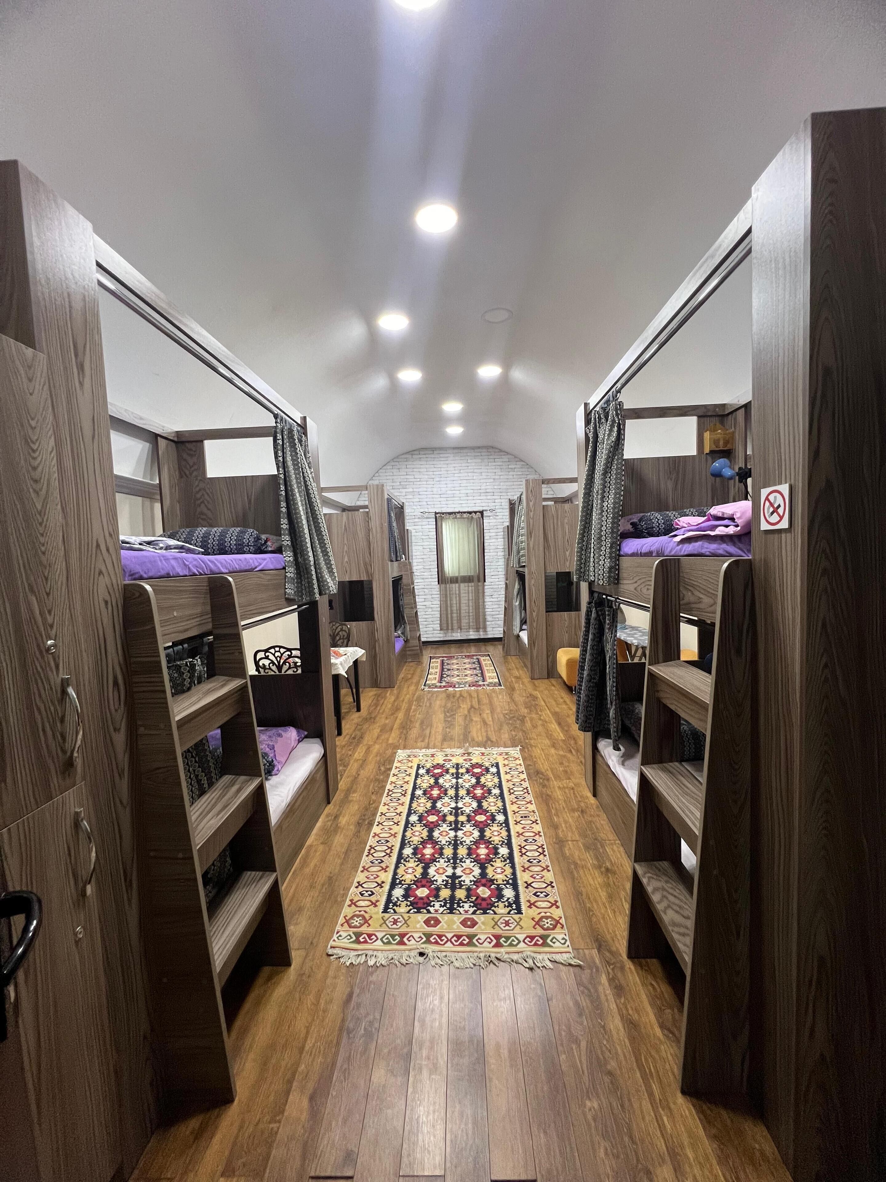 Ein Schlafsaalzimmer mit Etagenbetten, Holzschränken, einem gemusterten Teppich und einer Ziegelwand.