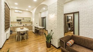A modern kitchen with white brick walls, wooden flooring, and a dining area with a table and chairs. - Salam Old Baku Hostel (Baku)