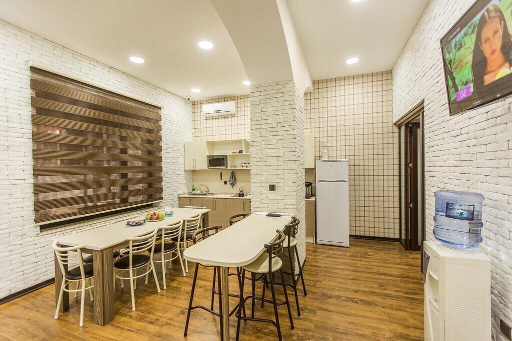 A compact kitchen with a dining area, white brick walls, a large window with blinds, and a water dispenser.