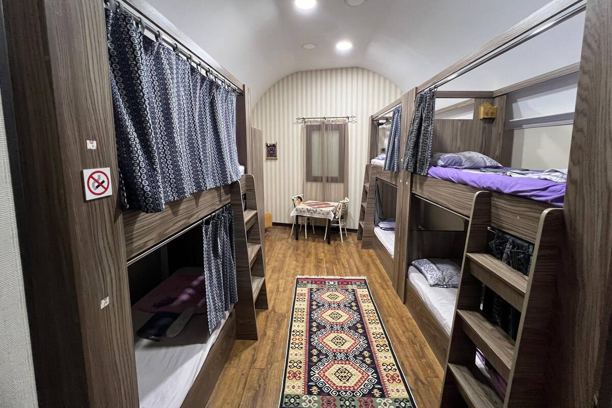 Una habitación pequeña con literas, una mesa compacta y una alfombra estampada.