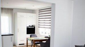 Una sala de estar moderna con piso de madera, un sofá negro, un otoman verde y un comedor con mesa y sillas.