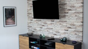 Una sala de estar moderna con un televisor de pantalla plana montado en una pared con diseño de ladrillo, un mueble de madera debajo y un cuadro en la pared.