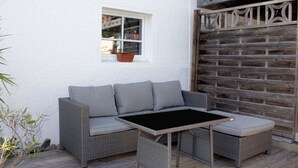 Un sofá de mimbre con cojines, una ventana pequeña con una planta en maceta y un portón de madera.