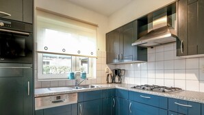 A modern kitchen with dark blue cabinets, a stainless steel range hood, a gas stove, and a built-in oven. - Luxurious Coastal Villa Near Forest (Sint Maartensvlotbrug)