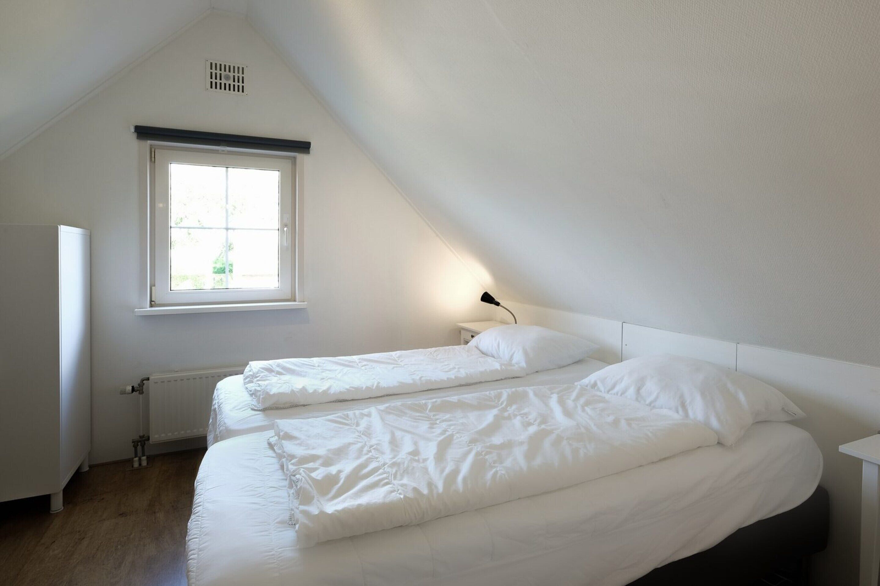 Una habitación pequeña y blanca, con dos camas, una ventana y un radiador.