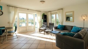 A living room with a sofa, chairs, a table, and a balcony with curtains. - Luxurious Coastal Villa Near Forest (Sint Maartensvlotbrug)