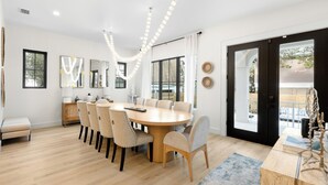 A modern dining area with a round table, six chairs, and a bench. There are large windows, a door leading outside, and a ceiling light fixture. - Upscale Seagrove Home + Private Pool & Golf Cart (Santa Rosa Beach)