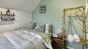 A bedroom with a bed, bedside tables, a hanging clothes rack, and a wall-mounted shelf with plants. - Cosy 2BDR Trafford Cottage, Fits 5, EV charger, WIFI, Parking 
 (Partington)