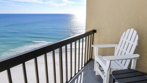 Un balcon avec un fauteuil Adirondack blanc et une petite table, donnant sur une plage et l’océan.