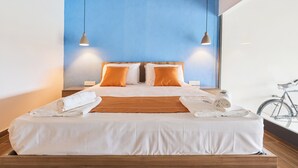 Habitació d'hotel moderna amb un llit gran, dos cossins, una bicicleta a la cantonada i una paret decorada de blau.