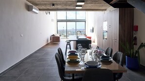 Una zona de dinar moderna amb una taula llarga per a sis persones, una vista de la ciutat a través de grans finestres i un sostre rústic.