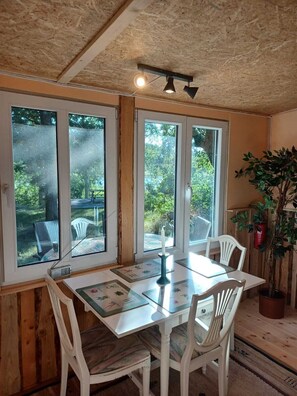 A dining area with a table, chairs, and large windows. - Cozy Stuga in the forest with lake view, close to Astrid Lindgren's World (Dalsebo)