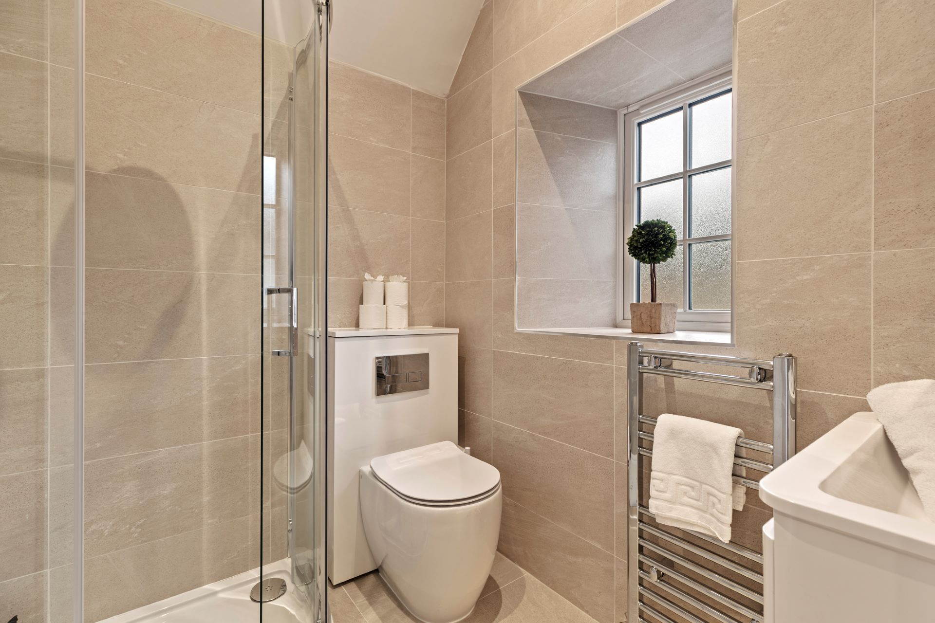 A modern bathroom with a glass shower enclosure, a toilet, a towel rack, and a window with a plant.