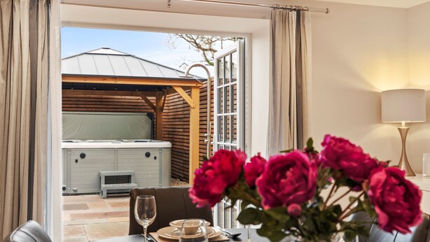 Un coin repas avec une table dressée pour deux personnes, un jacuzzi et, au fond, une pergola en bois.