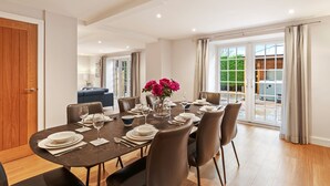 Un coin repas avec une table dressée pour six personnes, entourée de chaises, et une vue sur un jardin à travers des portes vitrées.
